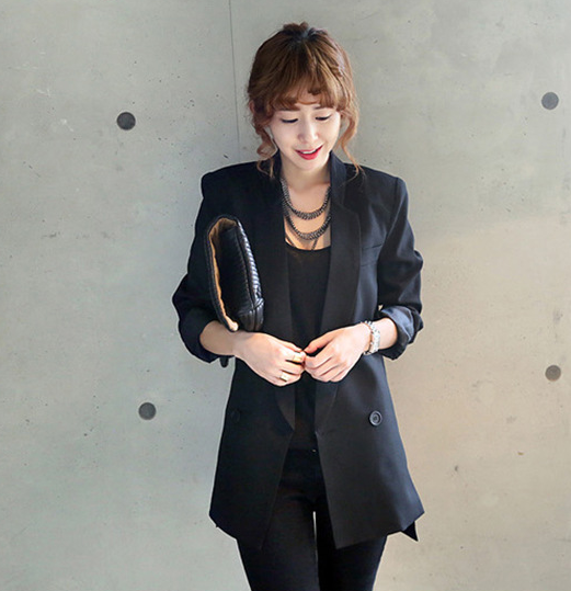 Woman wearing a black blazer holding a clutch against a plain background